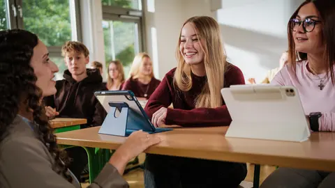 Schüler sitzen an einem Tisch mit Tablet in einem Klassenraum; daneben steht der Titel ‚Oberstufe & Abschlüsse am Gymnasium Elze‘.