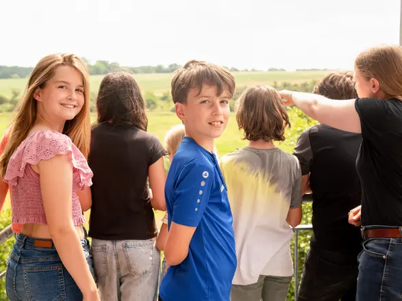 Gruppe von Jugendlichen steht auf einem Balkon und blickt lächelnd in die Natur. Zwei Jugendliche schauen in die Kamera, während andere auf die Landschaft zeigen. Das Bild vermittelt Gemeinschaft, Naturerlebnis und Freude am Miteinander.